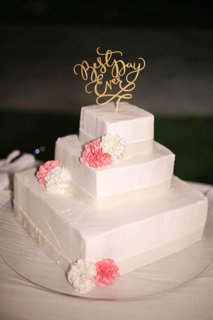 White beach wedding cake with pink and white peonies and gold topper